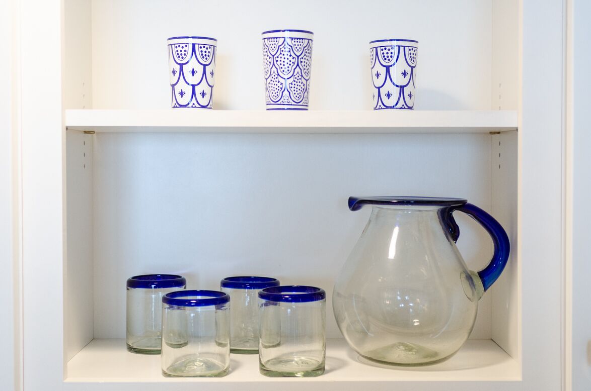 A shelf with three blue-patterned cups and a clear glass pitcher with a blue handle.