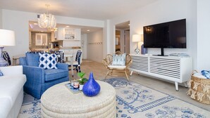Un salon moderne avec un canapé, un pouf et un téléviseur.
