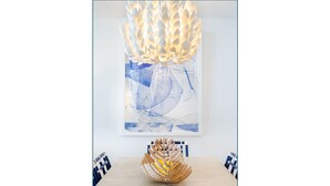 Un espace repas moderne avec une table en bois, des chaises bleues et blanches, un élément décoratif central et un grand tableau abstrait accroché au mur.