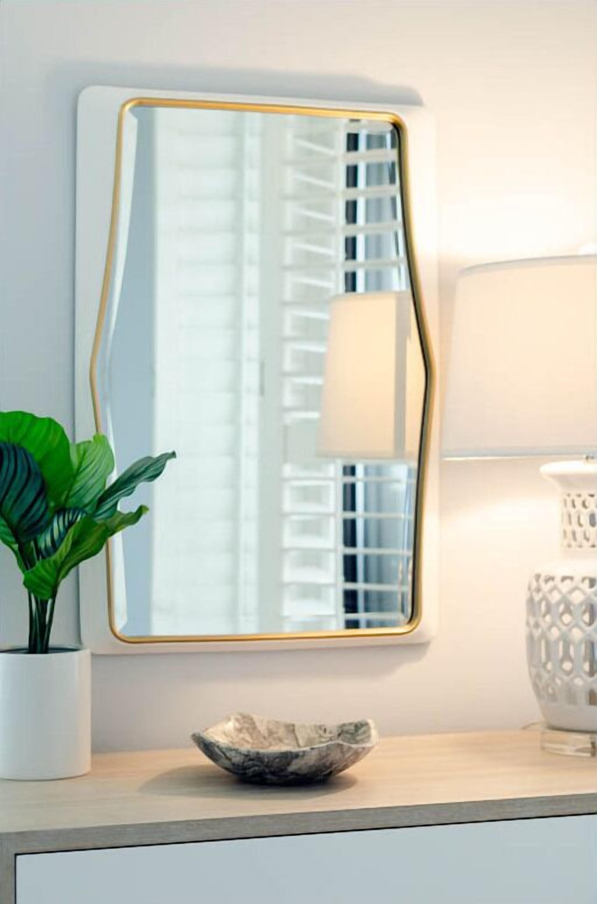 A mirror with a gold frame, a potted plant, and a decorative bowl on a dresser.