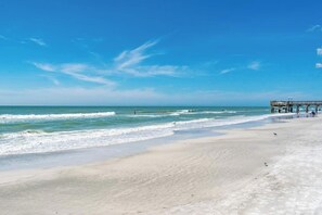 Een strand met een pier die zich uitstrekt over de oceaan, heldere lucht en rustige golven.