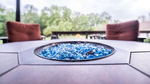 Una mesa hexagonal con una bandeja metálica llena de cubitos de hielo azules, ubicada al aire libre bajo una pérgola y con sillas rojas.