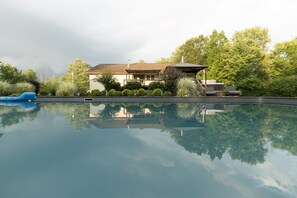 Ein Haus mit Schwimmbad, umgeben von Grünpflanzen und Bäumen.