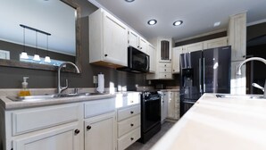 Una cocina moderna con armarios blancos, una estufa negra, un refrigerador de acero inoxidable y un microondas integrado.