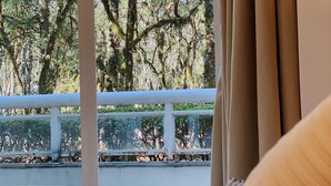 A bedroom with a view of trees through a window, a white railing, and a beige curtain.
