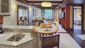 A modern hotel room with a kitchen area, dining space, and a living area with a sofa and TV.