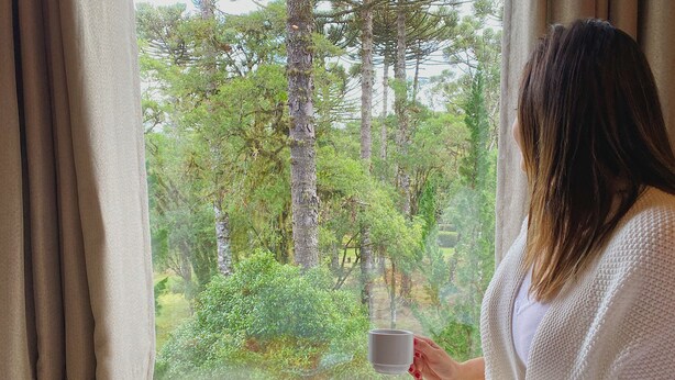 A woman sitting by a window with a tray of food and a cup.