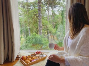 Una mujer sentada junto a una ventana, con una bandeja de comida y una taza.