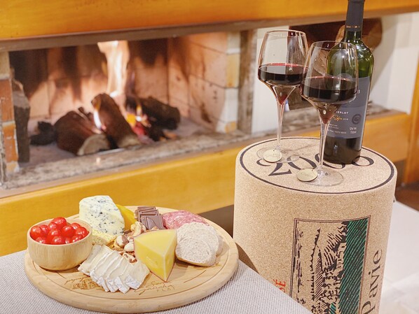 Una tabla de quesos con varios tipos de queso, nueces y uvas, una botella de vino y dos copas sobre una mesa redonda.