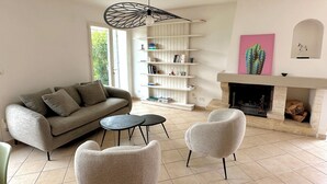 A living room with a sofa, two armchairs, a fireplace, a bookshelf, and a ceiling fan.