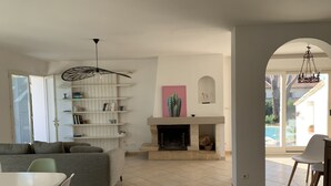 A spacious living area with a fireplace, a sofa, a dining table with chairs, and a bookshelf.