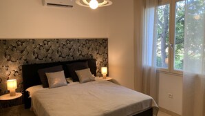 A bedroom with a bed, two bedside tables with lamps, a wall-mounted air conditioner, and a window with curtains.