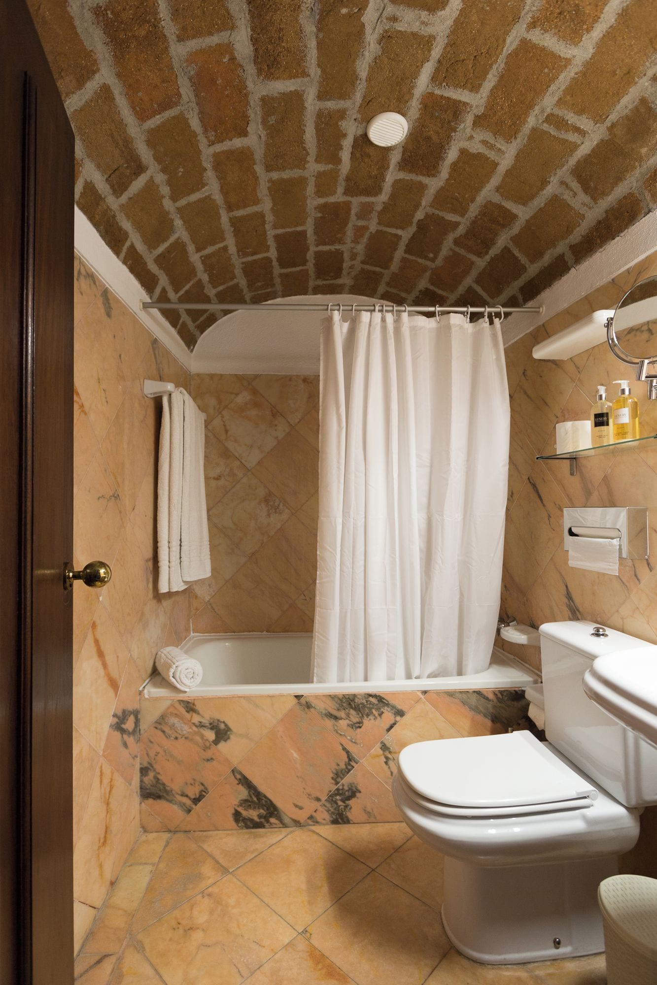 Bagno con doccia, WC e lavandino, caratterizzato da soffitto in mattoni e piastrelle in marmo.