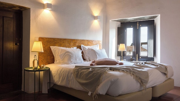 Un dormitorio con cama, lámparas de noche, mesita de noche y ventana con vistas.