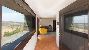 A corridor with a stone wall and a window overlooking a landscape. There is a yellow chair and a sofa in the room.