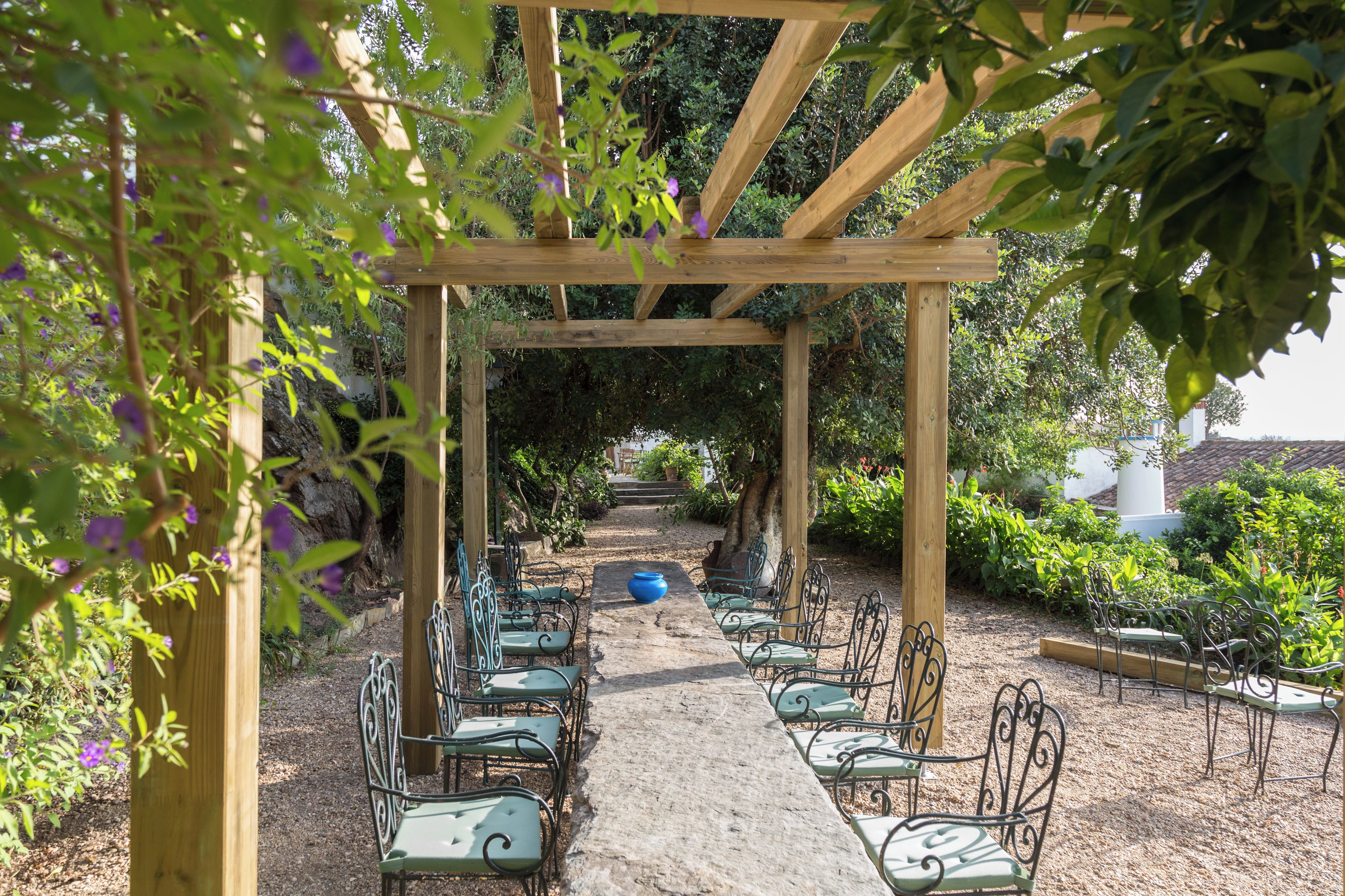 Una pérgola de madera con un camino de grava que lleva a una fila de sillas de metal verde.