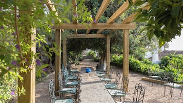 Una pérgola de madera con un camino de grava que lleva a una fila de sillas de metal verde.
