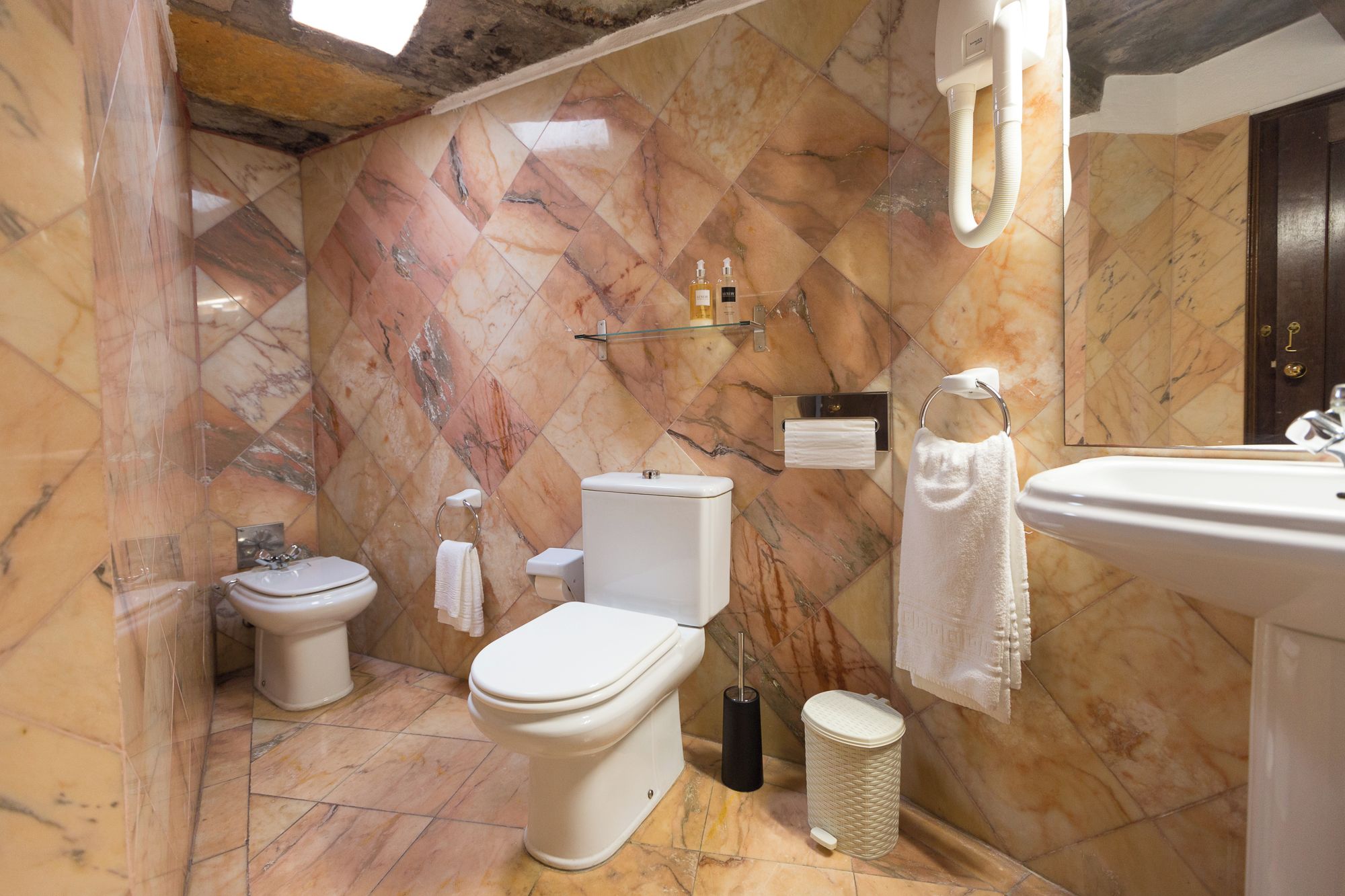 A bathroom with a toilet, bidet, and sink, marble walls, and a towel rack.