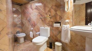 A bathroom with a toilet, bidet, and sink, marble walls, and a towel rack.
