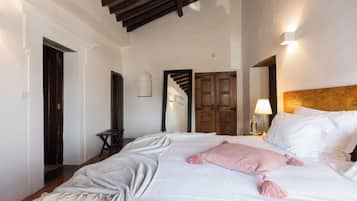 A hotel room with a bed, a wooden door, a mirror, and a lamp.