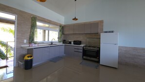 A modern kitchen with a gas stove, oven, and refrigerator. There is a window with curtains and a view of greenery outside.