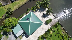 Vista aérea de un edificio con techo verde, rodeado de palmeras y una masa de agua.