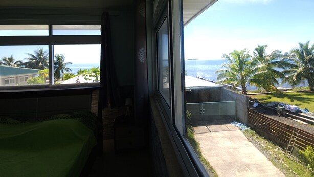 Una habitación con un ventanal grande que da a un balcón con vistas a palmeras y al océano.