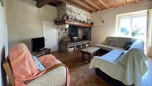 A cozy living room with a stone fireplace, a sofa, a chair, and a television. - GITE DU BOSC - LYS - Gîte (LYS)