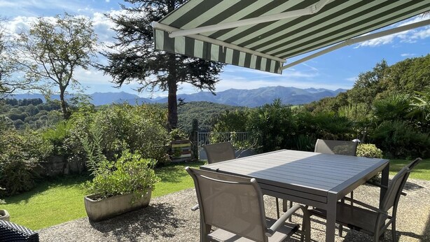An outdoor patio with a table and chairs, surrounded by greenery and a view of mountains. - GITE DU BOSC - LYS - Gîte (LYS)