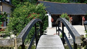A wooden bridge leading to a building with a dark roof and a covered parking area. - LE Mouly/petit Gite - Miossens-lanusse (MIOSSENS-LANUSSE)