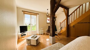 A spacious room with a large window, a flat-screen TV, a white sofa, a small table, and a wooden staircase. - LE Mouly/petit Gite - Miossens-lanusse (MIOSSENS-LANUSSE)