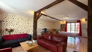 Een woonkamer met een rode leren bank, een zwarte bank, een houten salontafel en een eethoek met een tafel en stoelen.