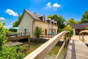 A rustic stone building with a wooden deck over a water channel, surrounded by greenery. - LE Mouly/grand Gite - Miossens-lanusse (MIOSSENS-LANUSSE)