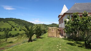 Una casa amb teulada inclinada, un pati tancat i vista a turons ondulats.