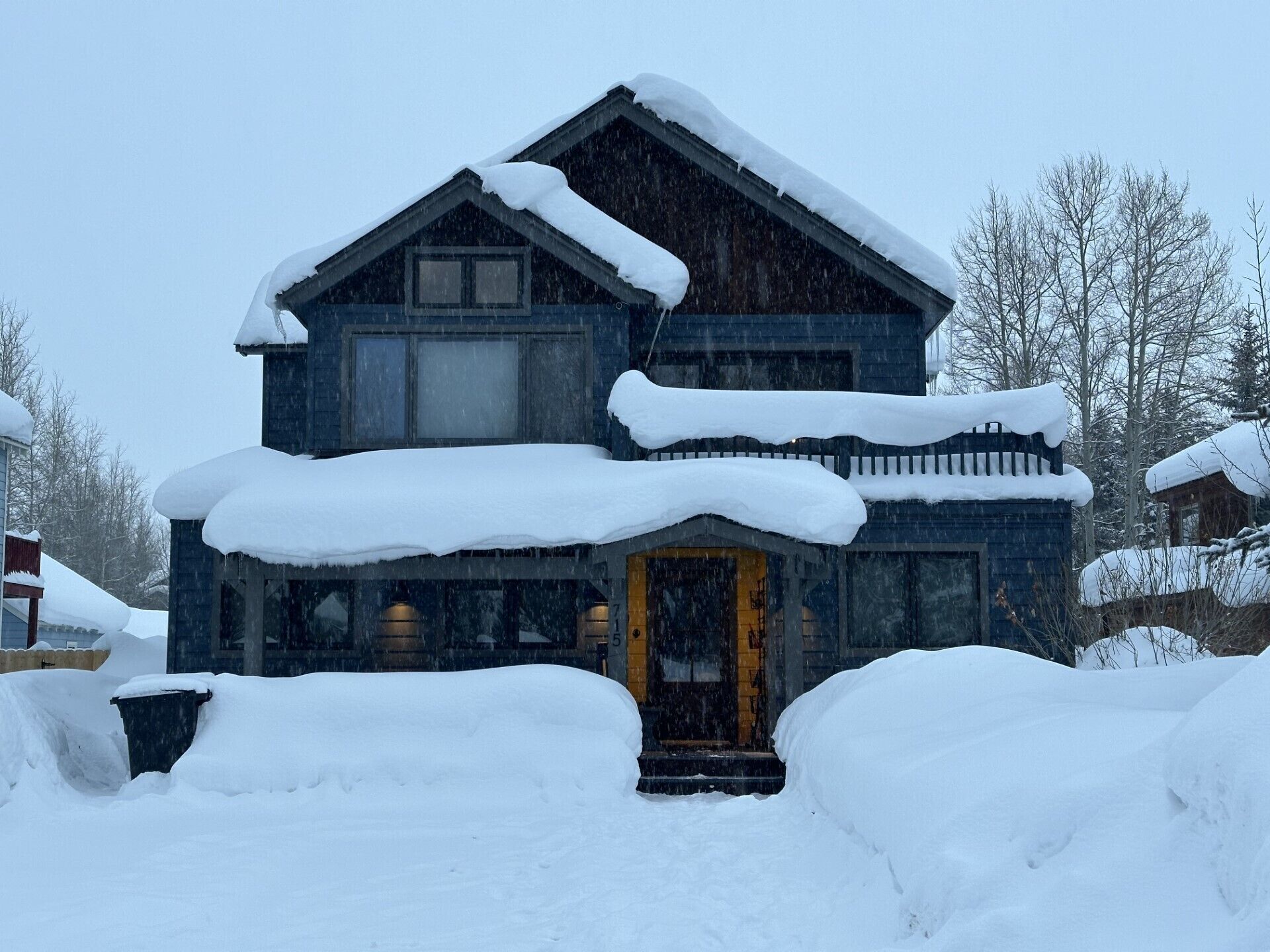 Une maison à deux étages, recouverte de neige, avec une porte d’entrée et des fenêtres bien visibles.
