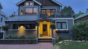 A two-story house with a prominent front entrance, a balcony on the upper floor, and a well-maintained front yard. - Crested Butte Home | 4 Bedroom | Hot Tub | Walk to Elk | Gas Grill |Pet-Friendly (Crested Butte)