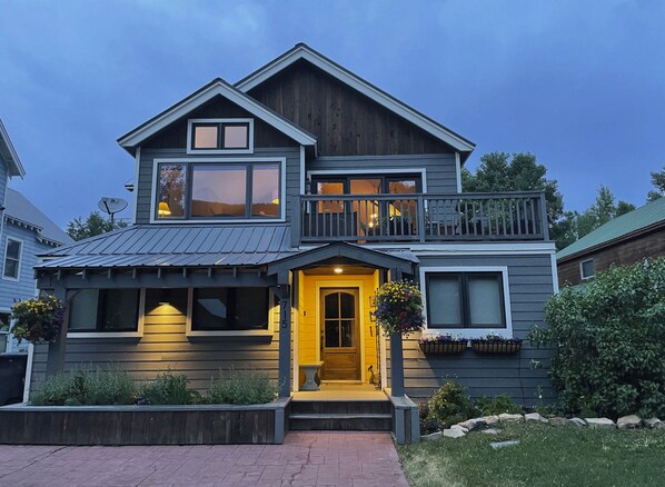 A two-story house with a prominent front entrance, a balcony on the upper floor, and a well-maintained front yard. - Crested Butte Home | 4 Bedroom | Hot Tub | Walk to Elk | Gas Grill |Pet-Friendly (Crested Butte)