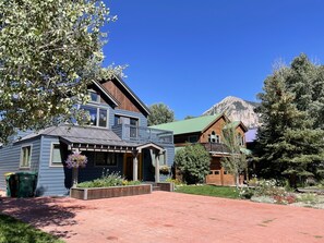 A two-story house with a front porch, a green roof, and a mountain in the background. - Crested Butte Home | 4 Bedroom | Hot Tub | Walk to Elk | Gas Grill |Pet-Friendly (Crested Butte)