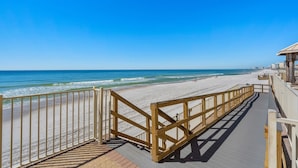 Une promenade en bois qui mène à une plage, avec un ciel bleu dégagé.