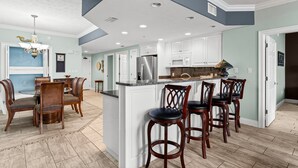 Una cocina moderna con armarios blancos, una isla central con taburetes y una zona de comedor con sillas de madera.
