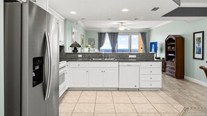 Una cocina moderna con armarios blancos, un refrigerador de acero inoxidable, un lavavajillas integrado y una ventana con cortinas.