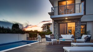 A modern outdoor pool area with lounge chairs and a two-story building with a balcony. - Atlantis Gardens Resort (Mazotos)