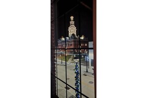 A view of a building with a prominent tower, through a window with a metal grid.