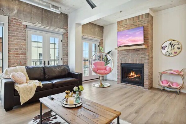 A living room with a brick wall, a fireplace, a TV, and a leather sofa.