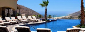 A luxurious pool area with lounge chairs and palm trees, overlooking a beach. - Beautiful Montecristo Villa - 3br/3.5 ba Sleeps 10 (Cabo San Lucas)