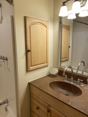 Un baño con tocador de madera, un lavabo con espejo y una lámpara sobre el espejo.