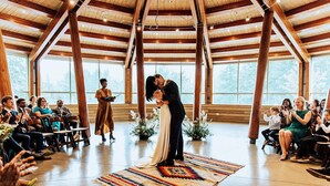 Una ceremonia de boda en un amplio salón con vigas de madera, ventanas grandes y un tapiz decorativo en el suelo.