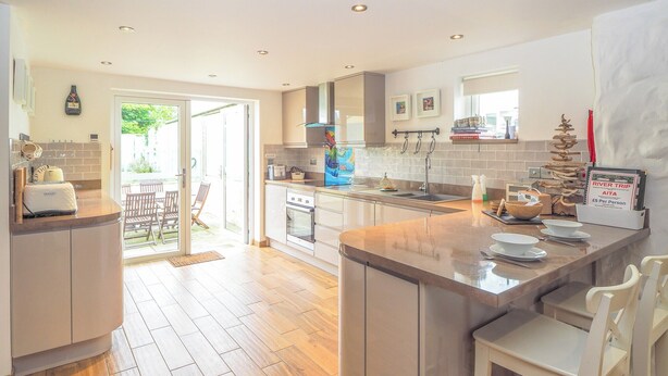 A modern kitchen with wooden flooring, a central island, and a dining area with white chairs. - 3 bedroom accommodation in Rhoshill, near Cardigan (Rhoshill, near Cardigan)