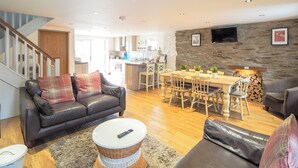 A modern living room with a leather sofa, a dining table, and a kitchen in the background. - 3 bedroom accommodation in Rhoshill, near Cardigan (Rhoshill, near Cardigan)