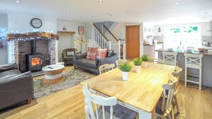 A modern living room with a fireplace, a dining area with wooden furniture, and a kitchen with white cabinets. - 3 bedroom accommodation in Rhoshill, near Cardigan (Rhoshill, near Cardigan)